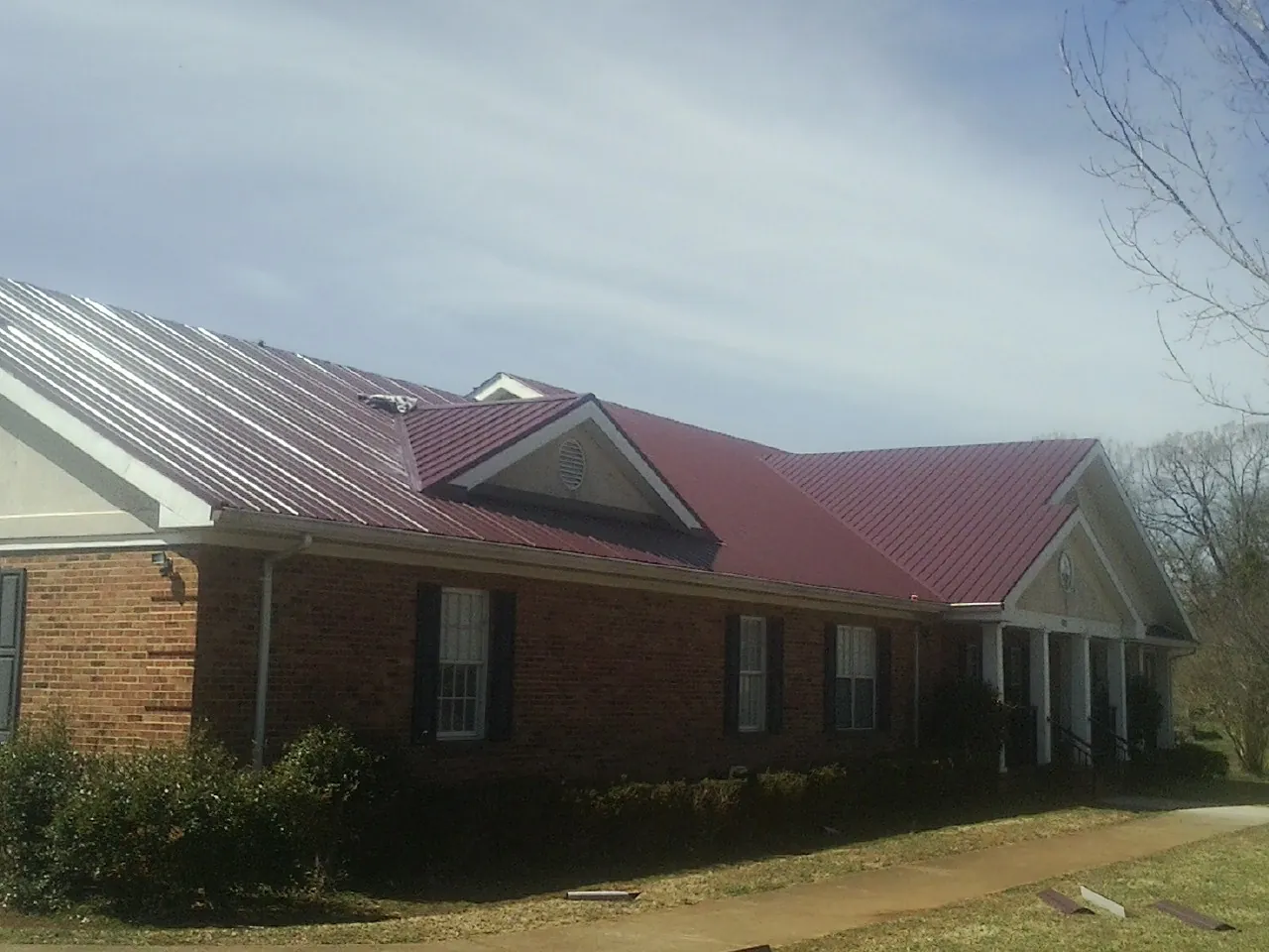 Red metal roof with gabled entries on a long brick building, from a Hail Damage Roof Repair job in Round Mountain