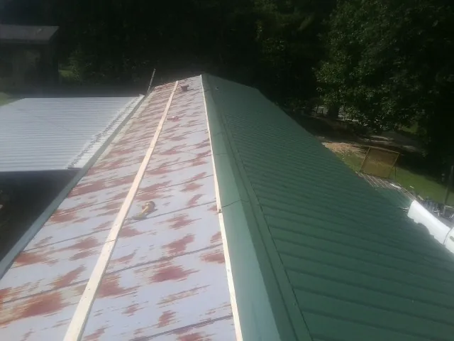 Old rusted panels beside newly installed green metal roofing — Wind Damage Roof Repair by Roofing Brothers in Round Mountain