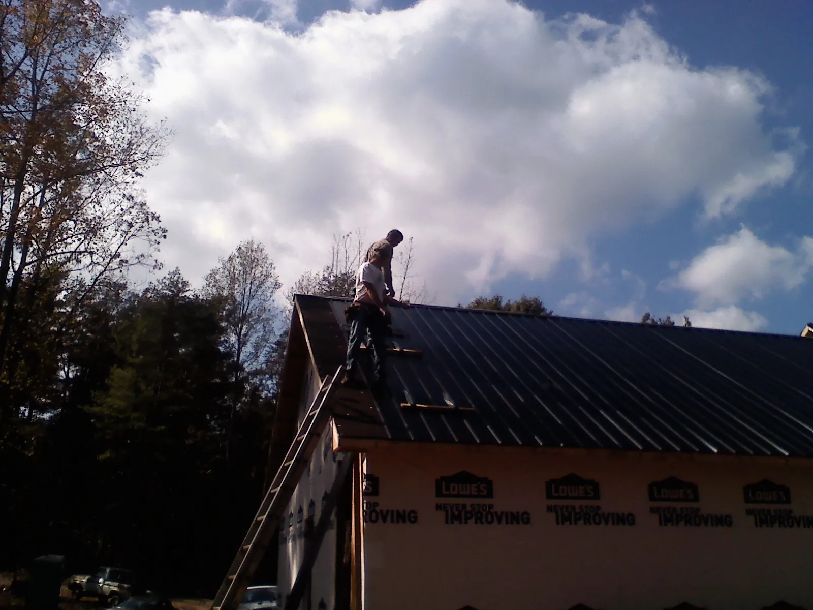 Roofer fastening dark metal panels high against a cloudy sky, from a Roof Inspection job in Round Mountain